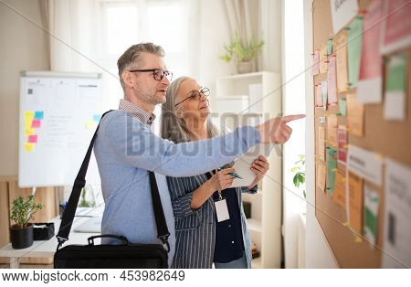 Recrutiment Agency Employee Standing In Front Of Employment Noticeboard And Helping Mature Man Searc