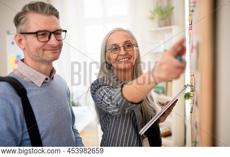Recrutiment Agency Employee Standing In Front Of Employment Noticeboard And Helping Mature Man Searc