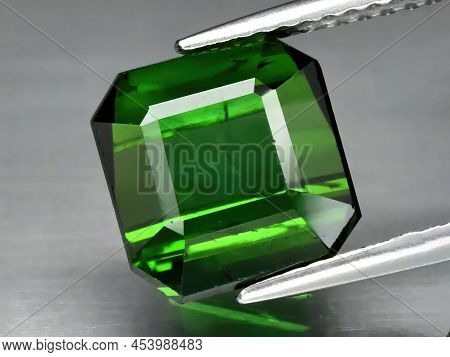 Natural Gemstone Green Tourmaline In Tweezers On A Gray Background