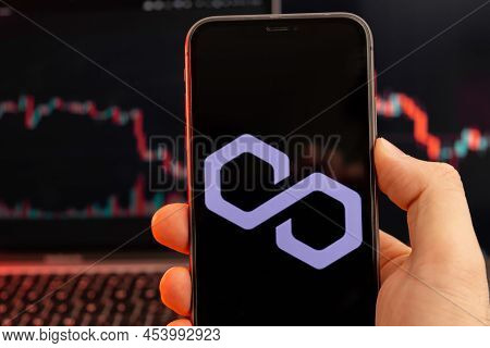 Polygon Matic Cryptocurrency Logo On The Screen Of Smartphone In Mans Hand With Downtrend On The Cha