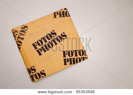 Vintage photo album cover made from burlap with stamped on terms Fotos and Photos printed on it laying on a table.