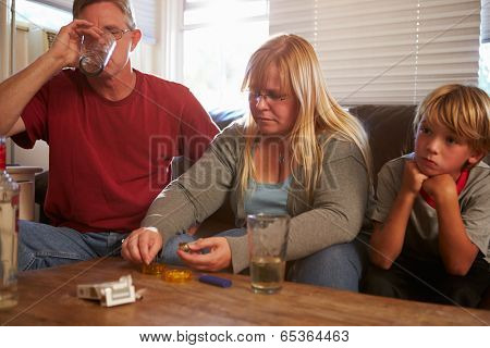 Parents Sit On Sofa With Children Taking Drugs And Drinking