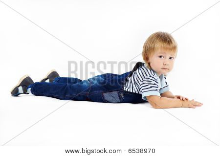 Het kleine jongetje in overall ligt op een vloer