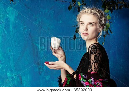 Young beautiful woman with blond hair in braids romantic hairstyle enjoying cup of coffee against blue painted grunge wall with space for text