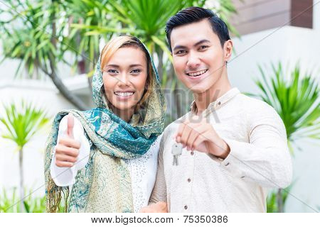 Asian Muslim man and woman moving into house presenting latchkey or key