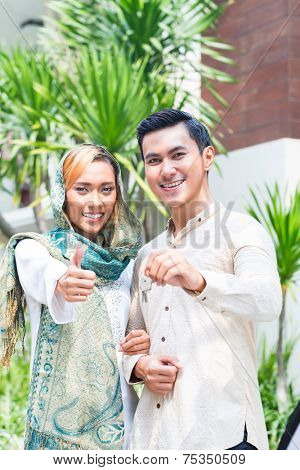 Asian Muslim man and woman moving into house presenting latchkey or key