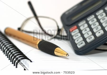 Notizbuch mit Stift, Rechner und Gläser.
