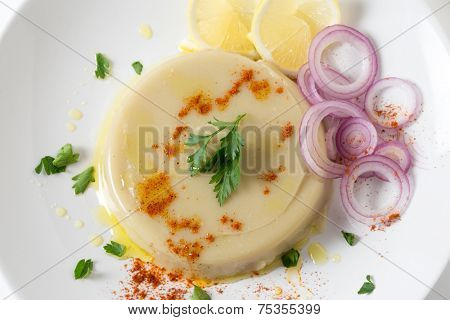 A pate of moulded Turkish dried fava bean puree, garnished with lemon, onion, paprika and parsley, kuru bakla ezmesi