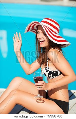 Happy young woman waffing and sitting close by swimming pool