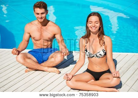 Young couple practicing yoga near swimming pool