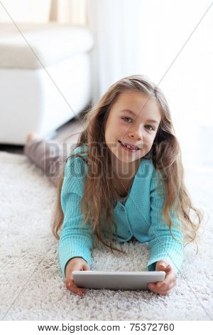 Child playing on ipad tablet pc sitting on a carpet at home