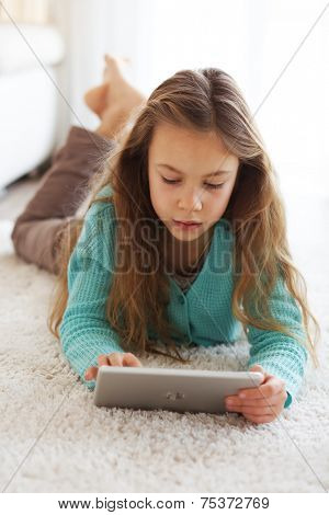 Child playing on ipad tablet pc sitting on a carpet at home