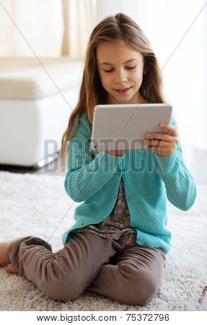 Child playing on ipad tablet pc sitting on a carpet at home