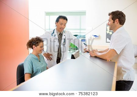 Doctor and nurse working on computer while man standing at reception desk in hospital