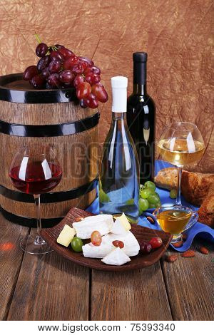Supper consisting of Camembert and Brie cheese, honey, wine and grapes on napkin in basket and wine barrel on wooden table on brown background