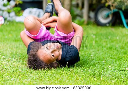 African girl playing on meadow in front of picket fence rolling around