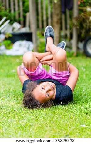 African girl playing on meadow in front of picket fence rolling around
