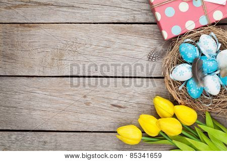 Easter background with blue and white eggs in nest, yellow tulips and gift box. Top view with copy space