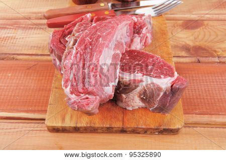 fresh raw uncooked beef fillet mignon entrecote on board prepared for cooking on wood table with cutlery and castors