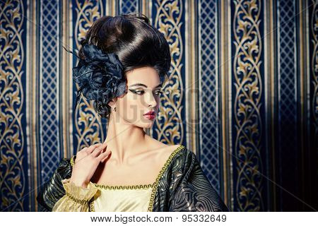 Baroque Style - beautiful young woman in elegant historical dress and with barocco hairstyle posing over vintage background. Renaissance. Barocco. Fashion.