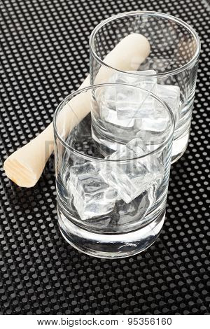 Cocktail glasses with ice and muddler on black rubber mat