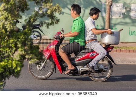HO CHI MINH CITY ( SAIGON ), VIETNAM, FEBRUARY 21, 2015 : A man is riding a motorbike , his friend is sitting at the opposite side holding a large kitchen recipient, Ho Chi Minh City, Vietnam
