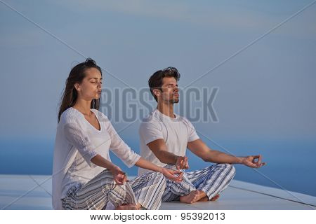 young couple practicing yoga at sunset in modern home terace with ocean and sunset in background