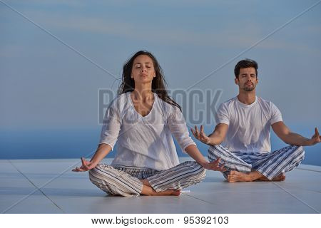 young couple practicing yoga at sunset in modern home terace with ocean and sunset in background