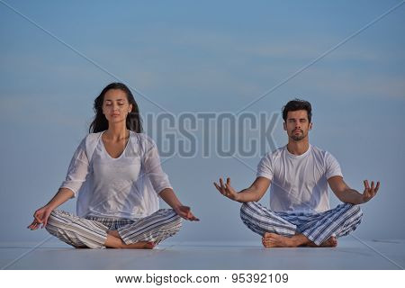 young couple practicing yoga at sunset in modern home terace with ocean and sunset in background