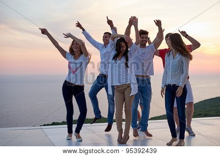 group of happy young people dancing and have fun on party in modern home bacony with sunset and ocean in background