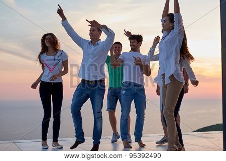 group of happy young people dancing and have fun on party in modern home bacony with sunset and ocean in background