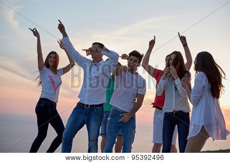group of happy young people dancing and have fun on party in modern home bacony with sunset and ocean in background