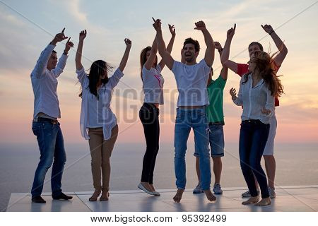 group of happy young people dancing and have fun on party in modern home bacony with sunset and ocean in background
