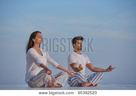 young couple practicing yoga at sunset in modern home terace with ocean and sunset in background