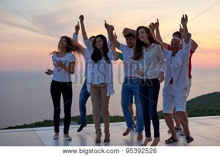 group of happy young people dancing and have fun on party in modern home bacony with sunset and ocean in background
