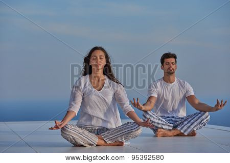 young couple practicing yoga at sunset in modern home terace with ocean and sunset in background