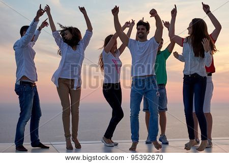 group of happy young people dancing and have fun on party in modern home bacony with sunset and ocean in background