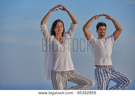 young couple practicing yoga at sunset in modern home terace with ocean and sunset in background