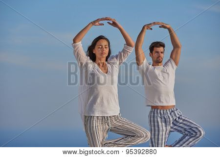 young couple practicing yoga at sunset in modern home terace with ocean and sunset in background