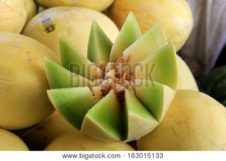 Honey Dew Melon cut open in pretty pattern, set on top of several
other whole melons at local farmers market.