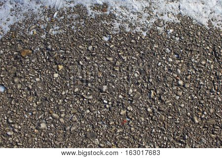 This is an abstract pattern of gravel in asphalt with snow on the upper fringe of the page.