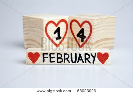 Valentine's day composition with wooden calendar. Handwritten February 14th, red hearts. Bright background.