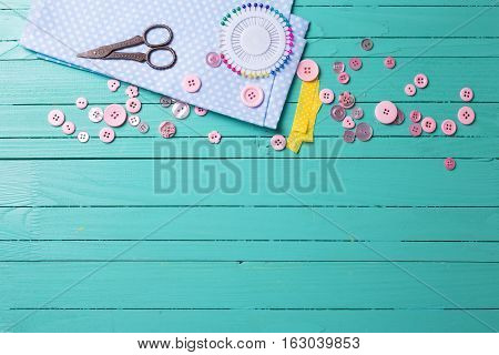 Sewing thread - buttons scissors fabric on turquoise wooden background. Selective focus. Scrapbboking. Flat lay. Place for text.