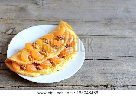 Sweet omelet on the plate and on wooden table with copy space for text. Fried omelet stuffed with fresh tangerines and walnuts. Vegetarian dessert. Breakfast omelette recipe