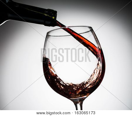 Grape wine poured from bottle into wine glass from glass on blank background