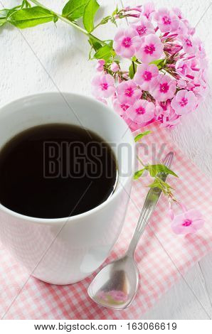 Morning coffee or cup of tea with pink flowers on wooden white rustic table. Selective Focus.