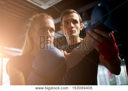 Young sportswoman trains in boxing with coach in hall
