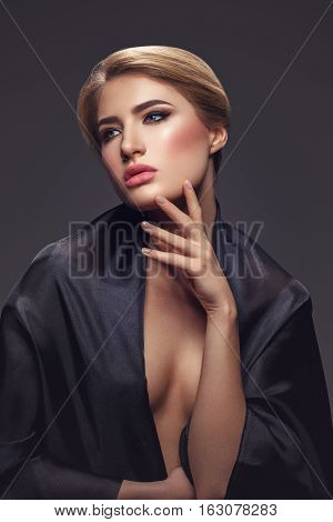 Portrait of beautiful young woman with cat eye make-up in black fabric. Studio beauty shot over black background.