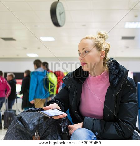 Casual blond young woman using her mobile phone while waiting to board a plane at airport departure gates.