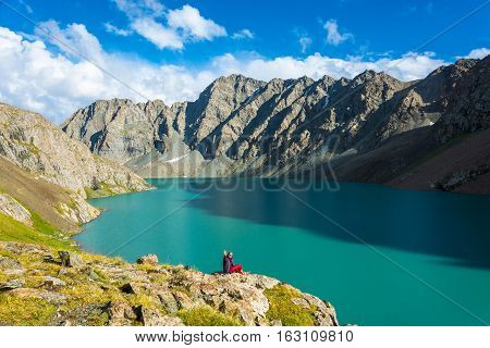 A Woman Sits On The Shore Of A Mountain Lake Ala-kul, Kyrgyzstan.